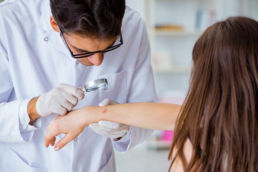 Hautarzt untersucht den Arm einr Patientin mit der Lupe